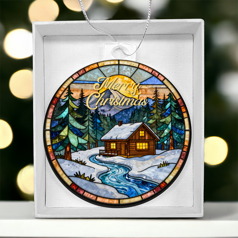 Round acrylic Christmas ornament displayed in a white gift box, featuring a stained-glass style print of a cozy winter cabin surrounded by pine trees with "Merry Christmas" written at the top.