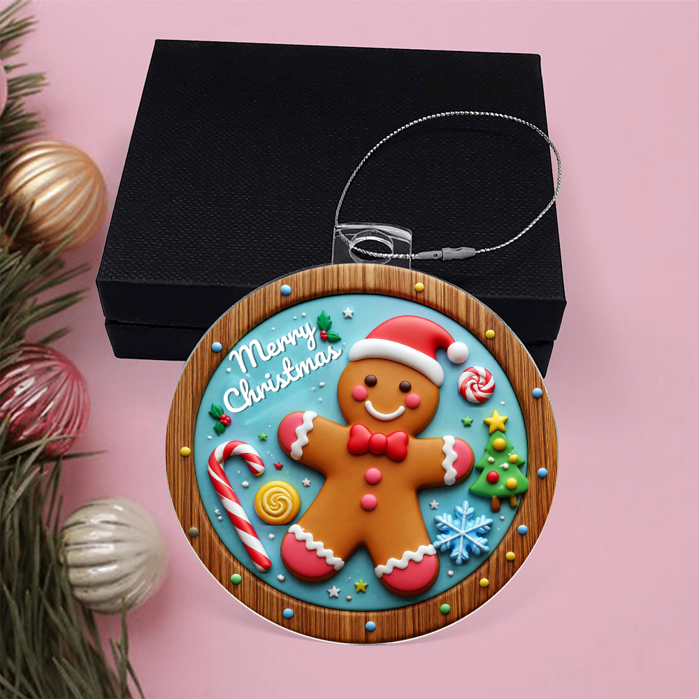 Round acrylic Christmas ornament in a stained-glass style featuring a cheerful, smiling gingerbread man surrounded by holiday sweets and "Merry Christmas" written at the top, set against a pink surface with a black gift box.