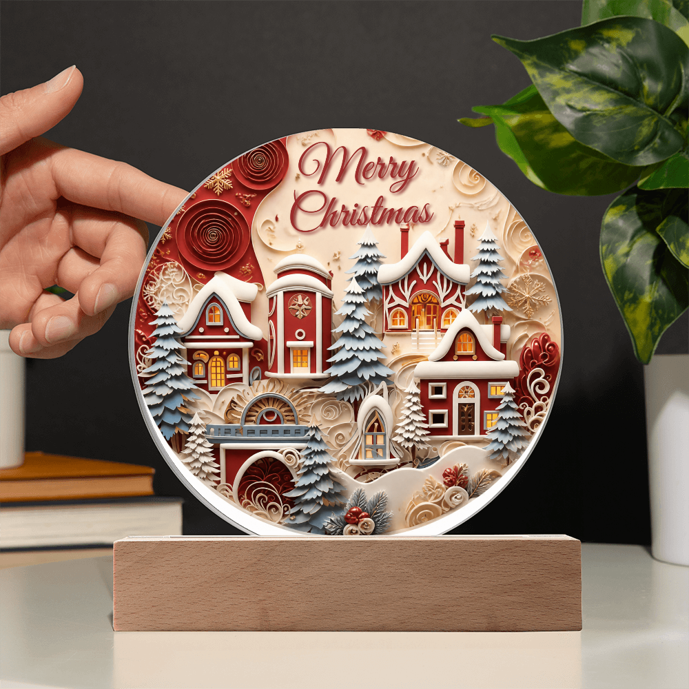 Hand holding a round acrylic Winter House Merry Christmas plaque on a wooden base with festive holiday decor in the background.