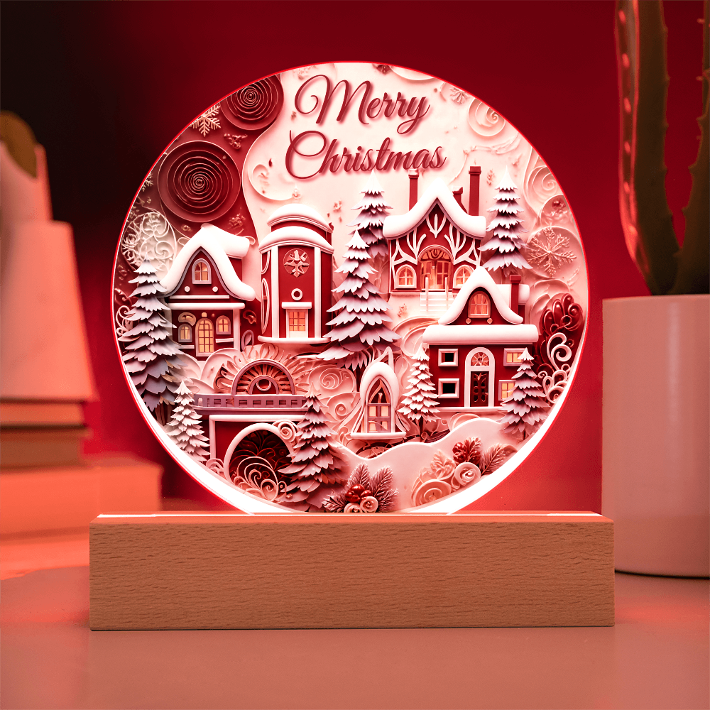 Winter House round acrylic desk plaque glowing with pink LED backlighting, featuring a snow-covered village and Merry Christmas text on a wooden base.