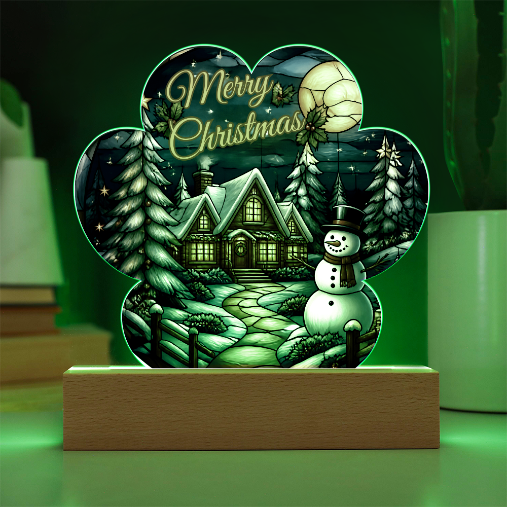 Illuminated paw-print acrylic Christmas ornament featuring a glowing winter cabin, snowman, and pine trees, displayed on a wooden LED base.